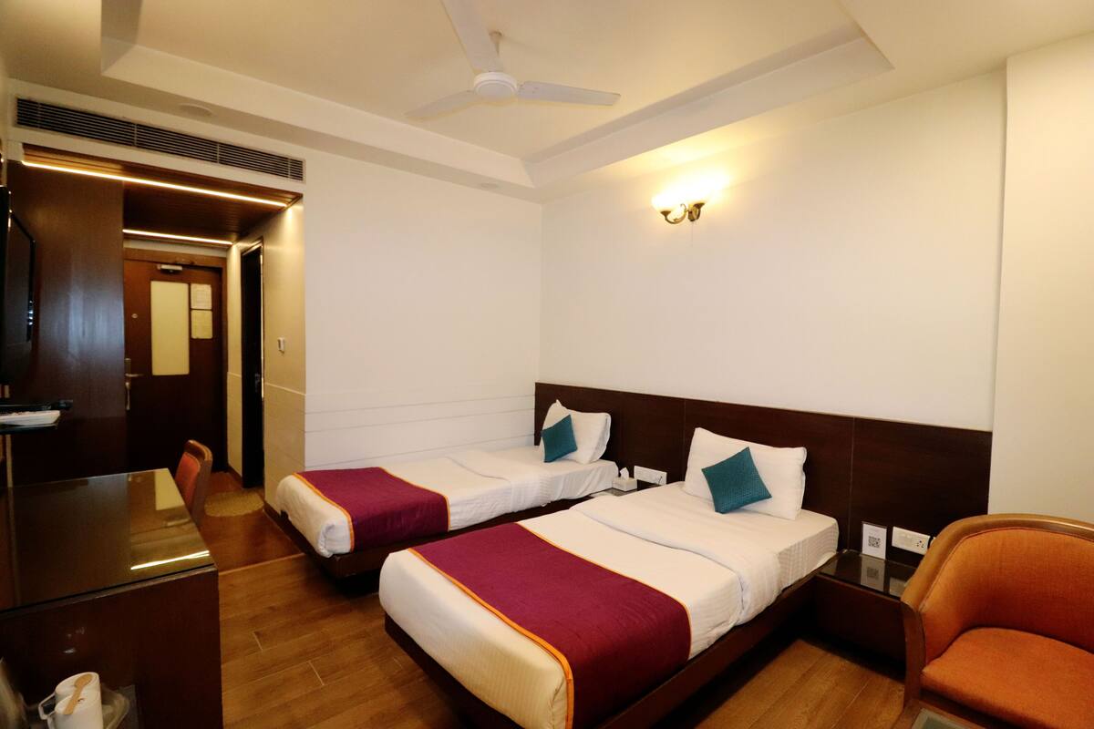 A hotel room with two beds, a desk, a chair, and a ceiling fan.