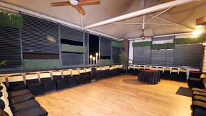 Un vaste espace extérieur aménagé avec un sol en bois, des bancs noirs rembourrés et une table recouverte d’une nappe foncée.