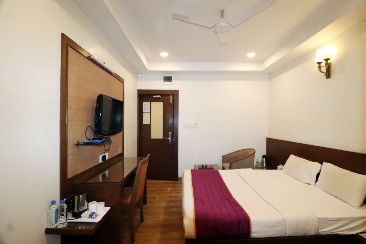 A hotel room with a bed, a desk with a chair, a television, and a ceiling fan.