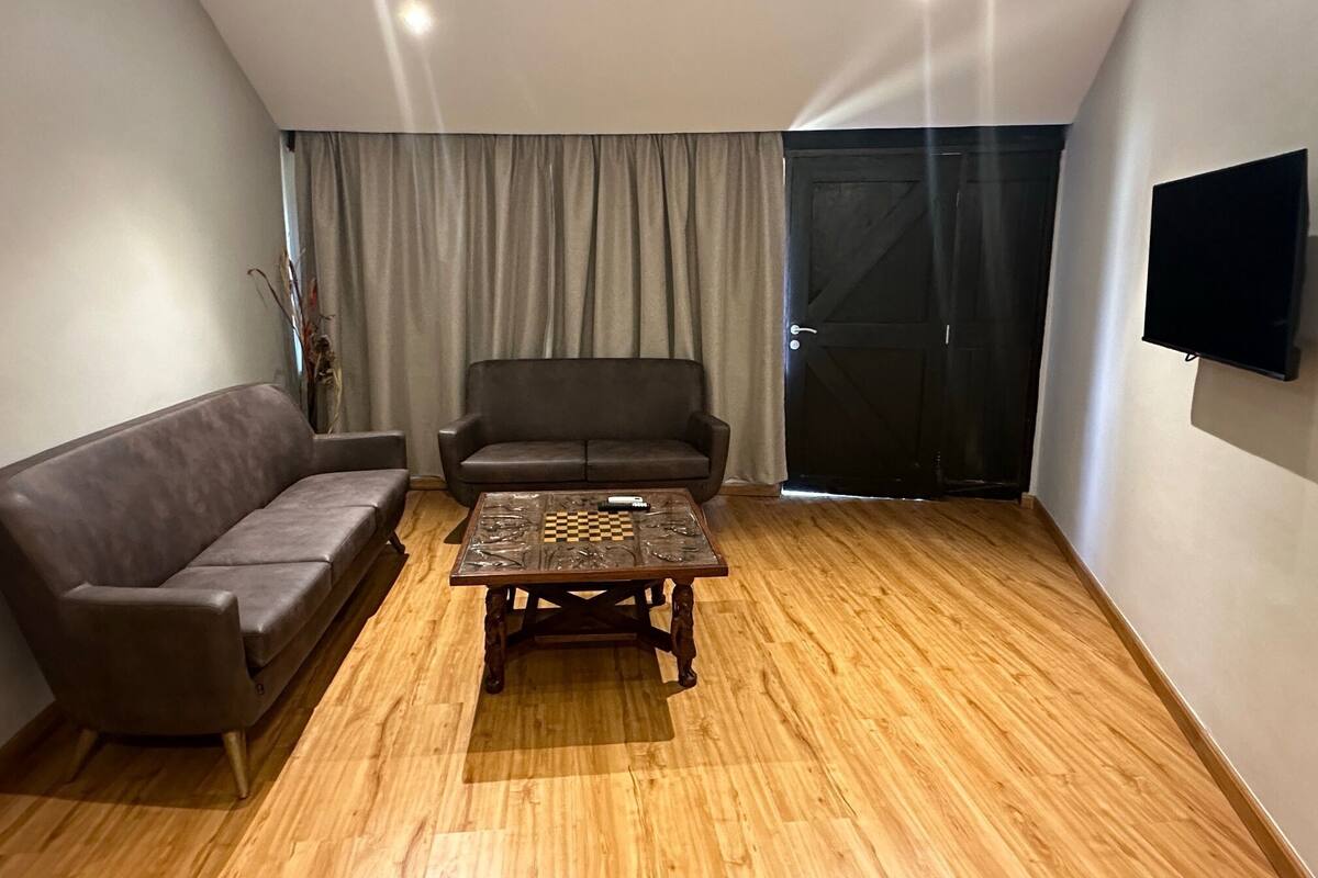 Una sala de estar con piso de madera, un sofá, una mesa de centro y un televisor montado en la pared.