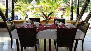 A dining table set for four with a vase of flowers, a bottle of water, and a menu.