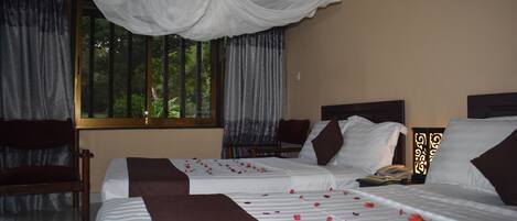 A hotel room with two beds, a canopy bed, a chair, a bedside table with a lamp, and a window with curtains.