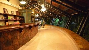 A curved reception area with a stone counter and tiled floor, leading to a glass wall with a view of greenery.