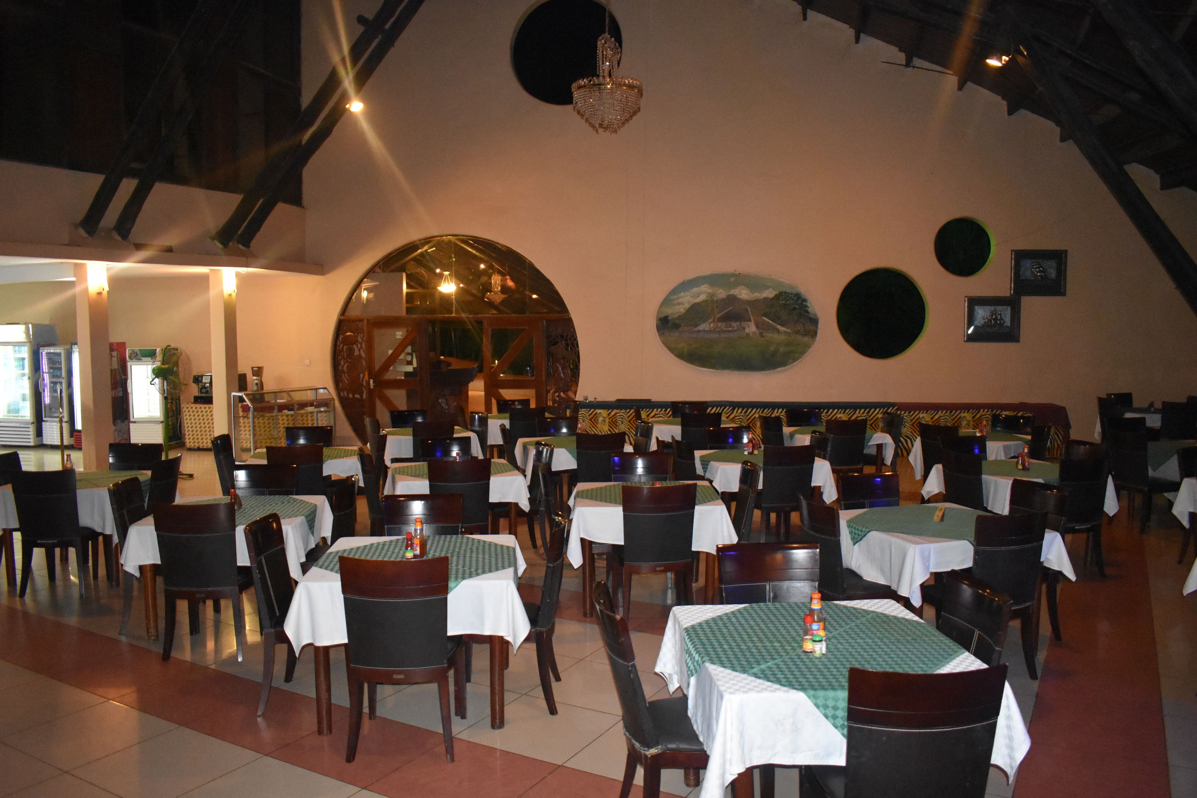 Un restaurante con varias mesas y sillas, un amplio ventanal arqueado y una lámpara de candelabro.