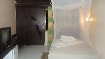 A room with a bed under a mosquito net, a television, and a wooden door.