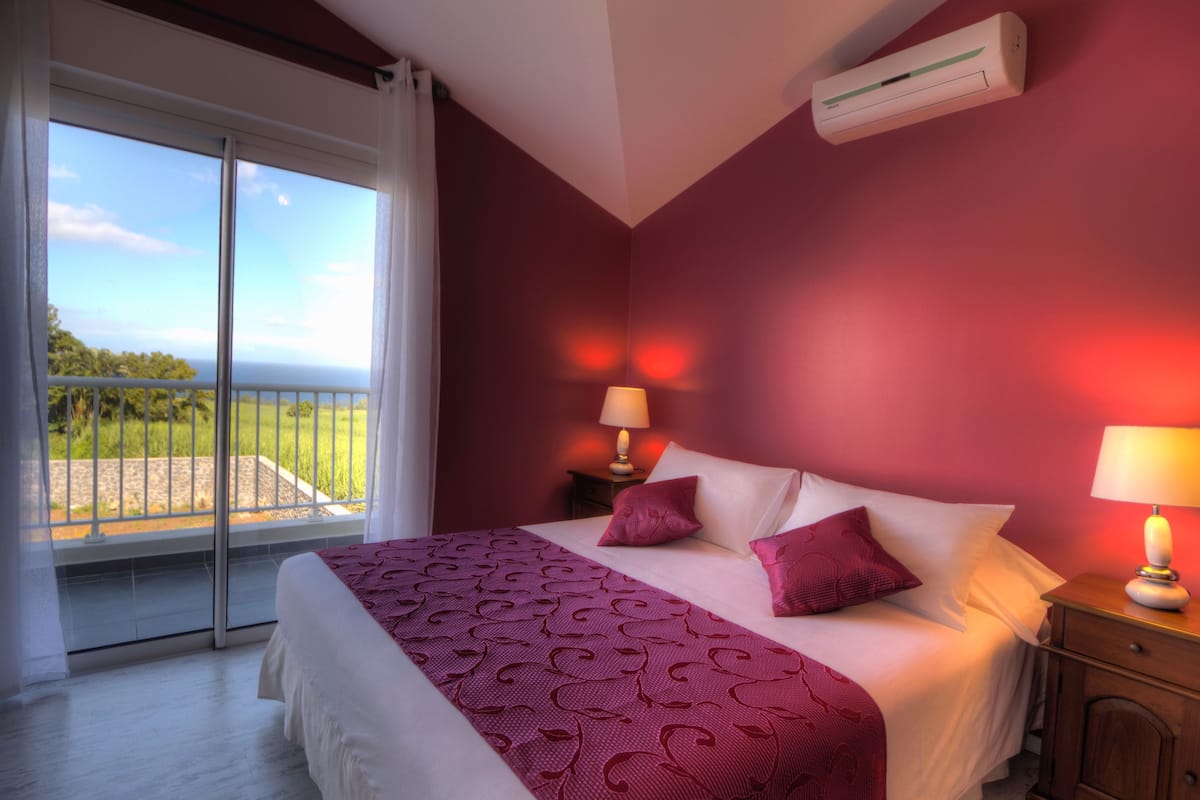 Habitación de hotel con cama, dos lámparas de noche, mesita de noche, puerta corrediza de vidrio a un balcón y un equipo de aire acondicionado en la pared.