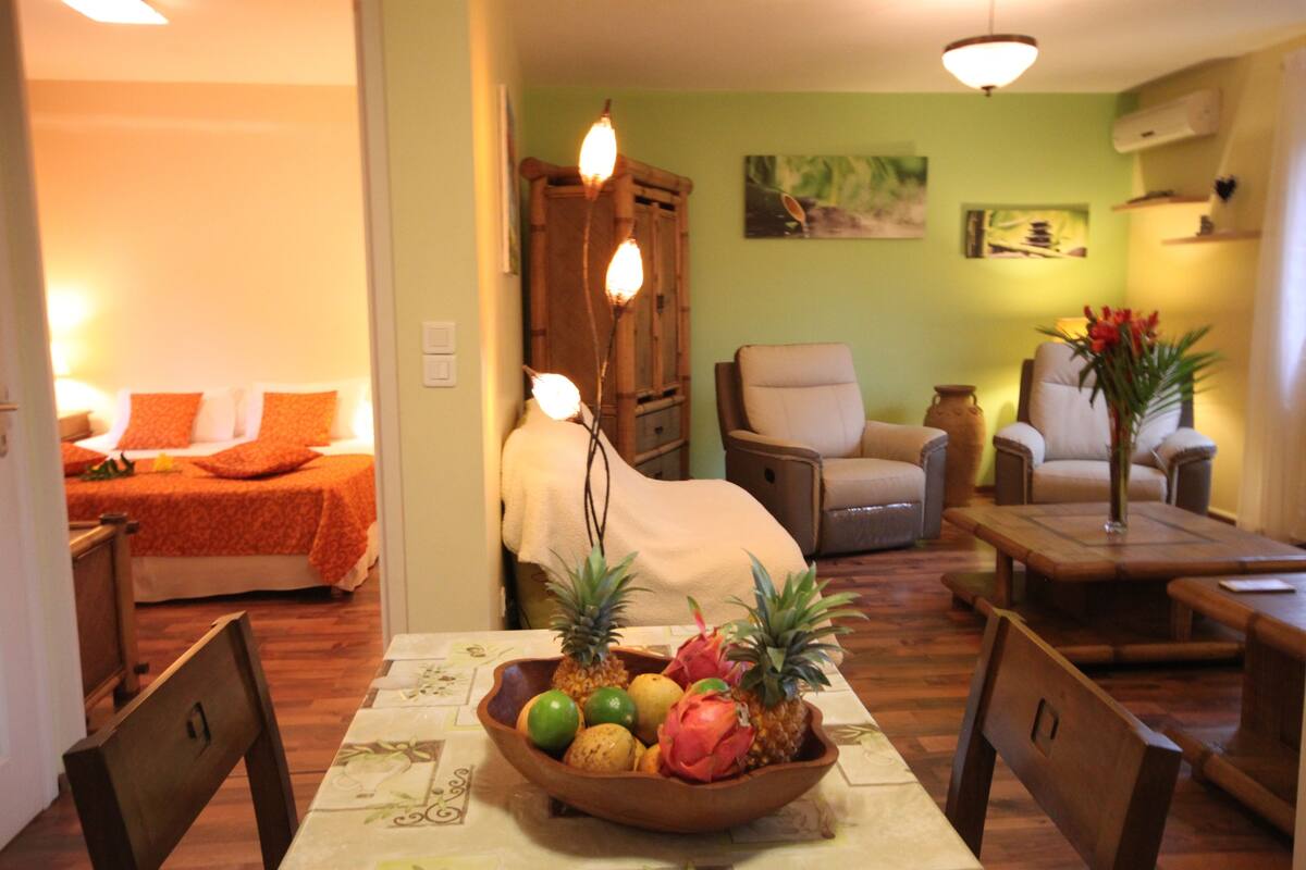 Un salón con una mesa de comedor en el centro, un sofá y una silla. Hay un mueble de madera y un cuadro en la pared.