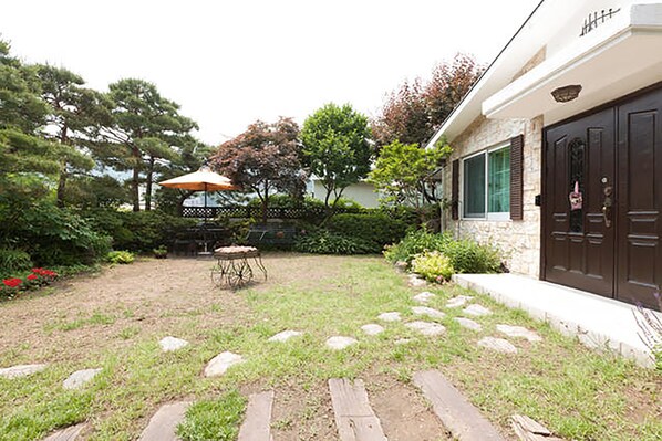 A residential backyard with a stone pathway, a wooden table, and an umbrella.