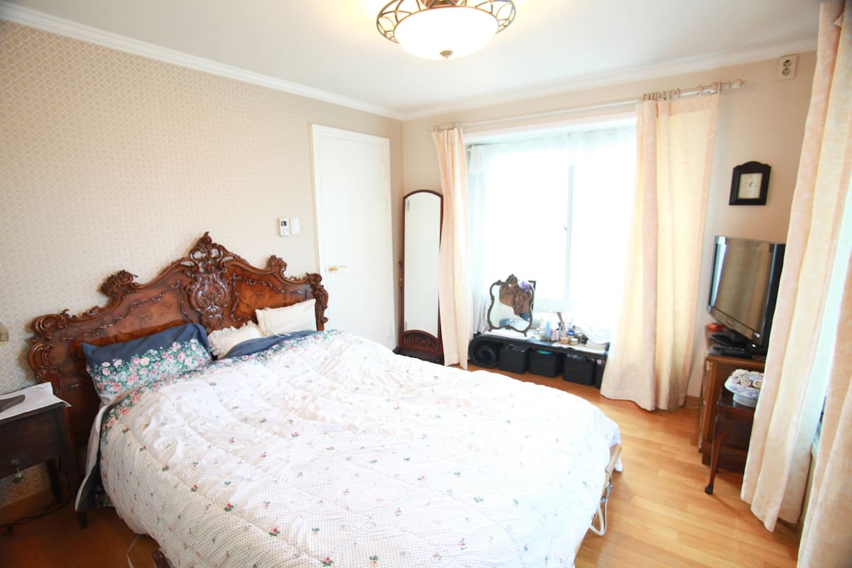 Un dormitorio con una cama grande, un aparador, un espejo, un televisor y una ventana con cortinas.