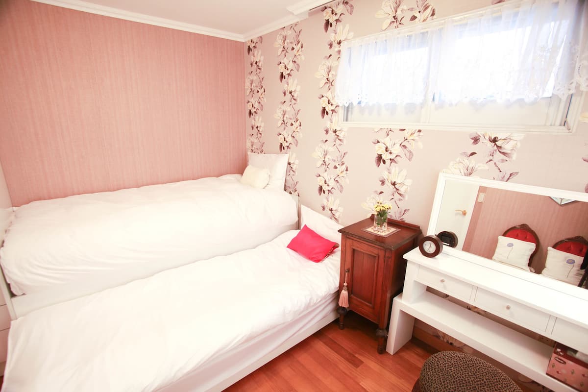 Un dormitorio con una cama doble, un pequeño aparador de madera, un espejo y un papel tapiz con motivos florales.