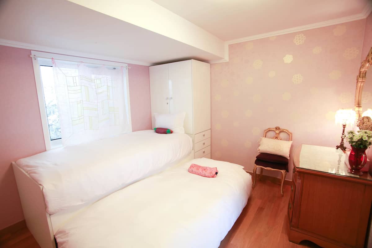 Un dormitorio con dos camas, un armario, una silla y una mesita de noche con lámpara.