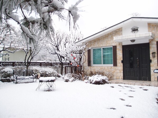 A stone house with a black door, a window with shutters, and a snow-covered lawn. - Cindy's B&B (Seoul)