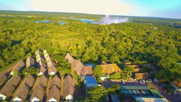 Vista aérea de un complejo turístico con cabañas de techo de paja, una piscina y un bosque denso que rodea la propiedad.