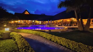 A resort with a swimming pool, lounge chairs, and a well-lit building at dusk.