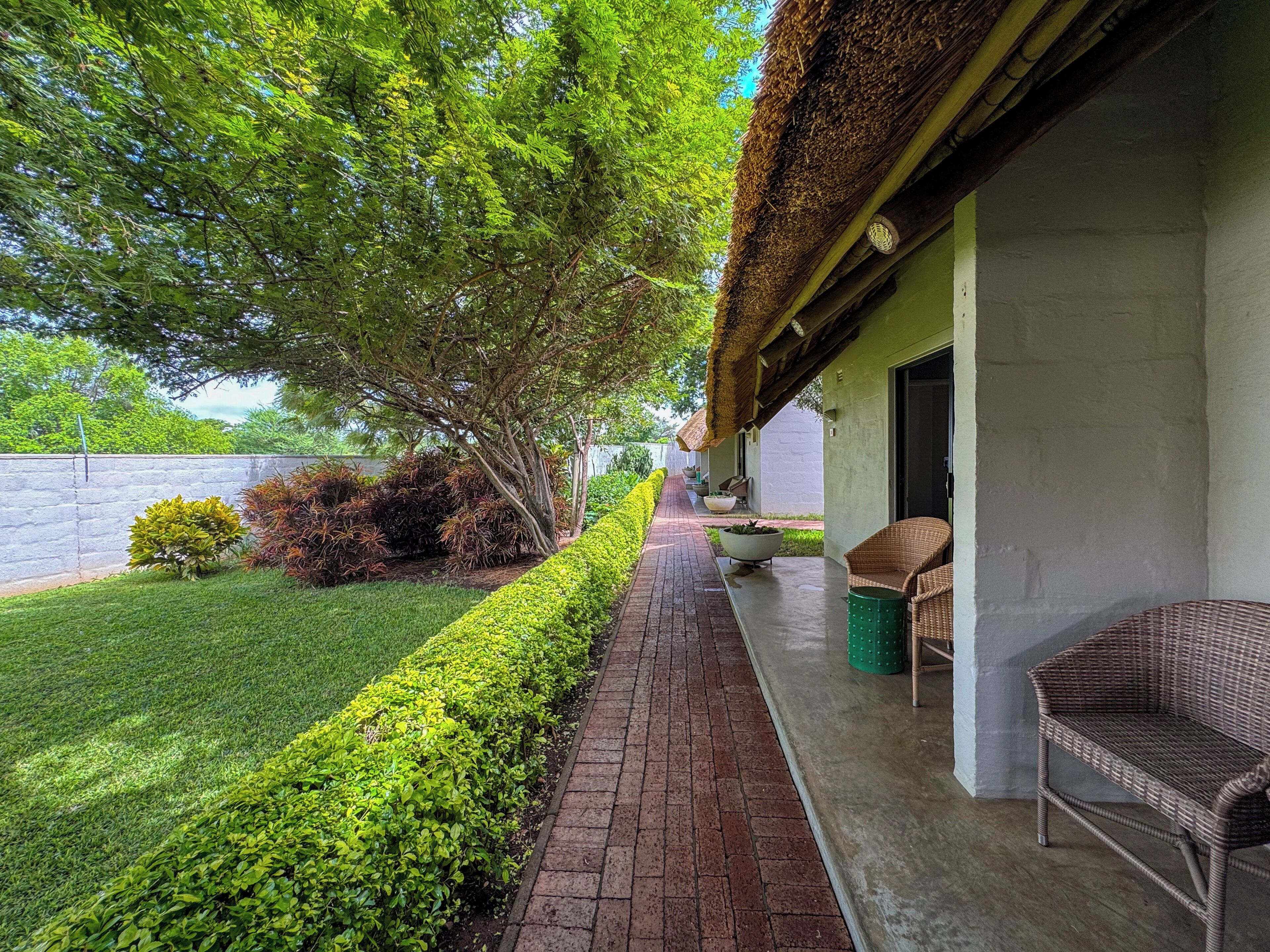 A covered outdoor area with a brick pathway, wicker furniture, and a well-maintained lawn.