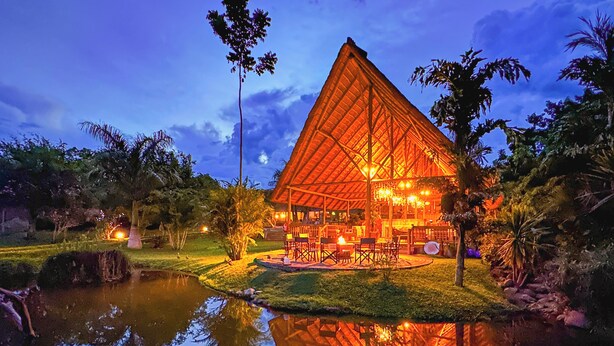 A large, triangular-roofed building with outdoor seating and a pond in front.