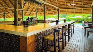 An outdoor bar area with a wooden deck, bar stools, and a thatched roof.