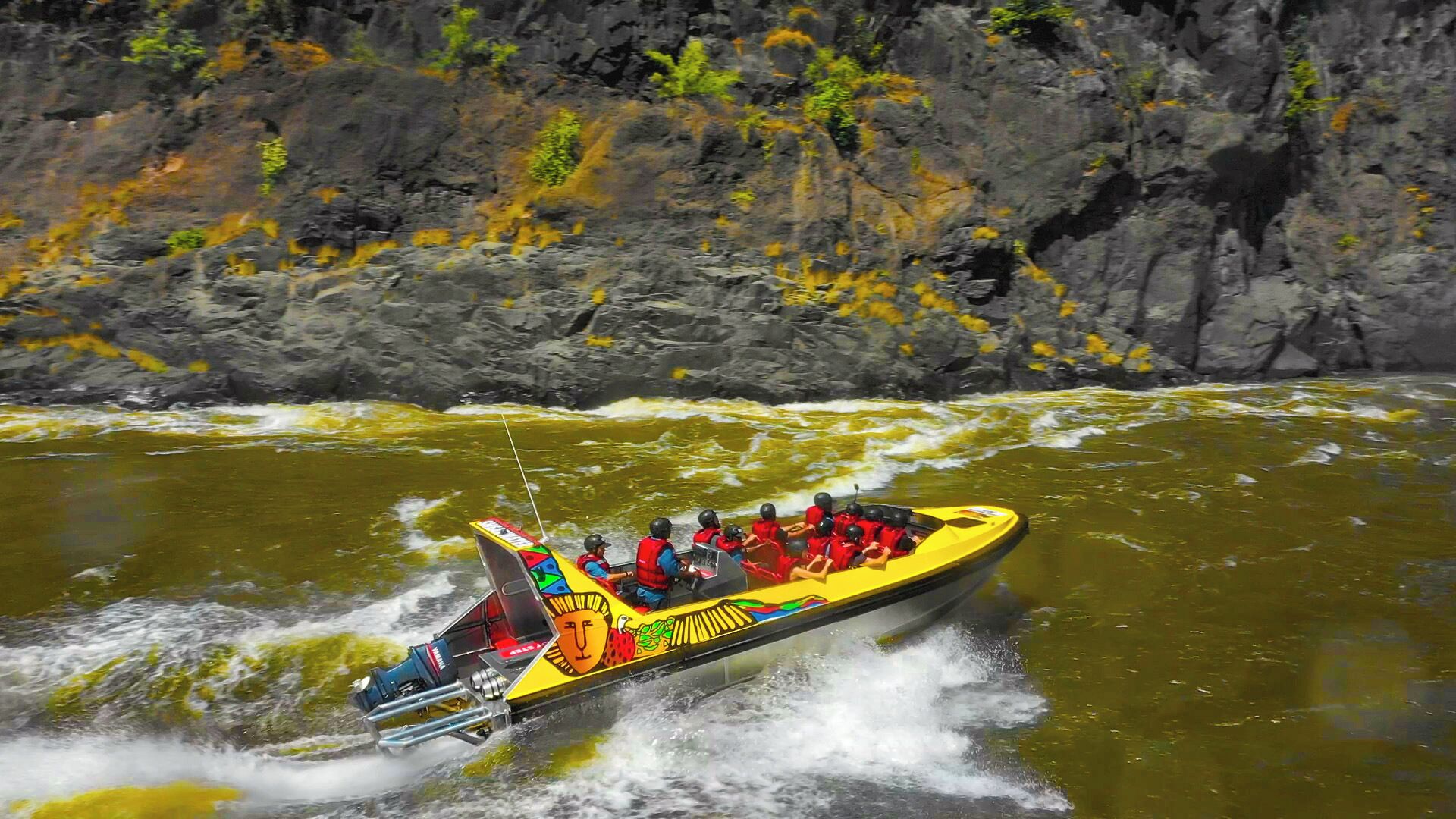 A yellow speedboat with passengers wearing life jackets, navigating through a river surrounded by rocky cliffs.