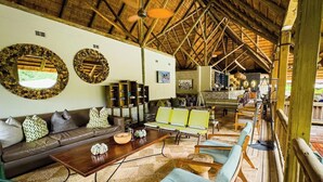A spacious lounge area with a high wooden ceiling, a sofa set, a coffee table, and a seating area with chairs.