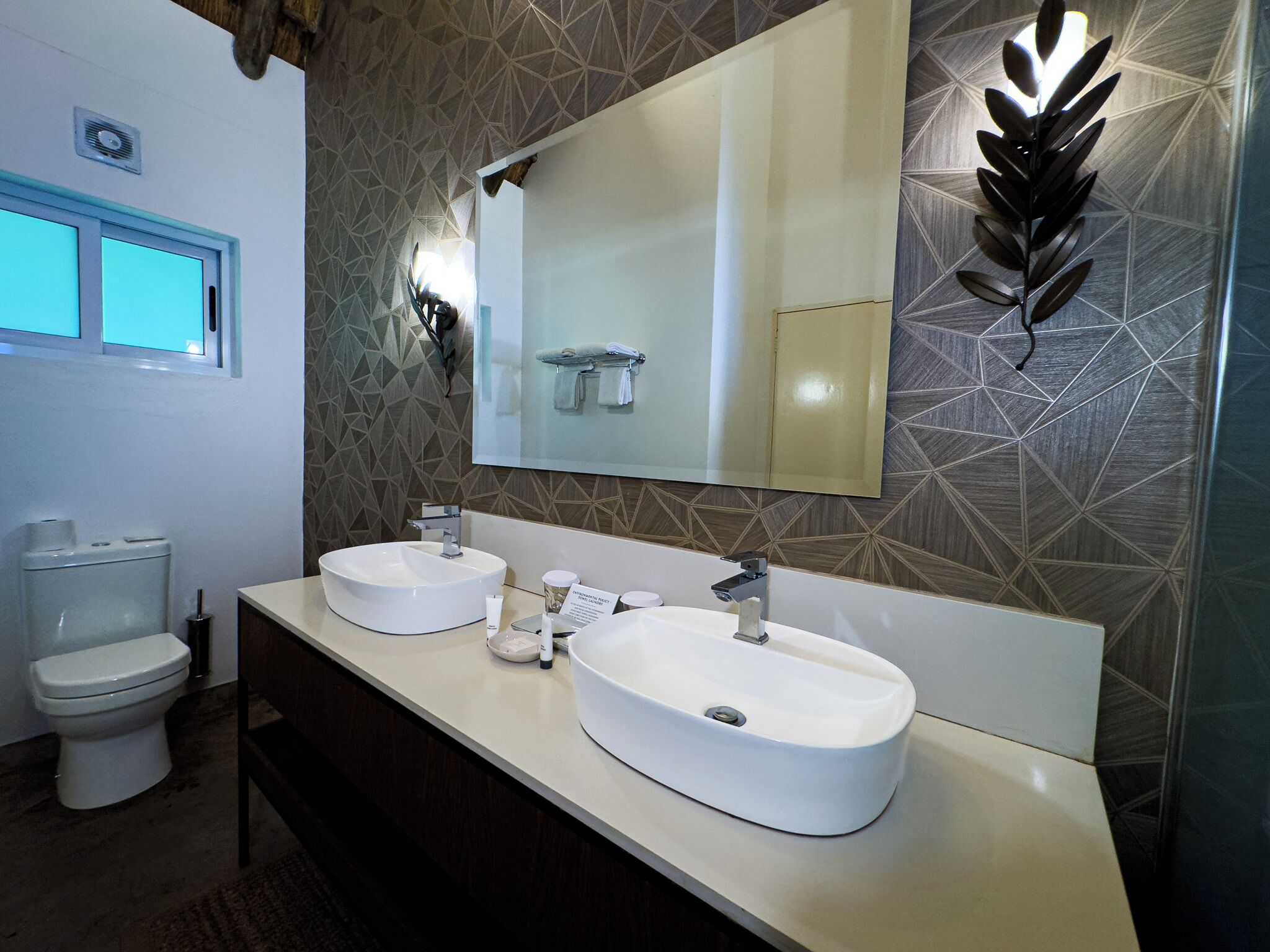 A modern bathroom with two sinks, a large mirror, and a geometric patterned wall.