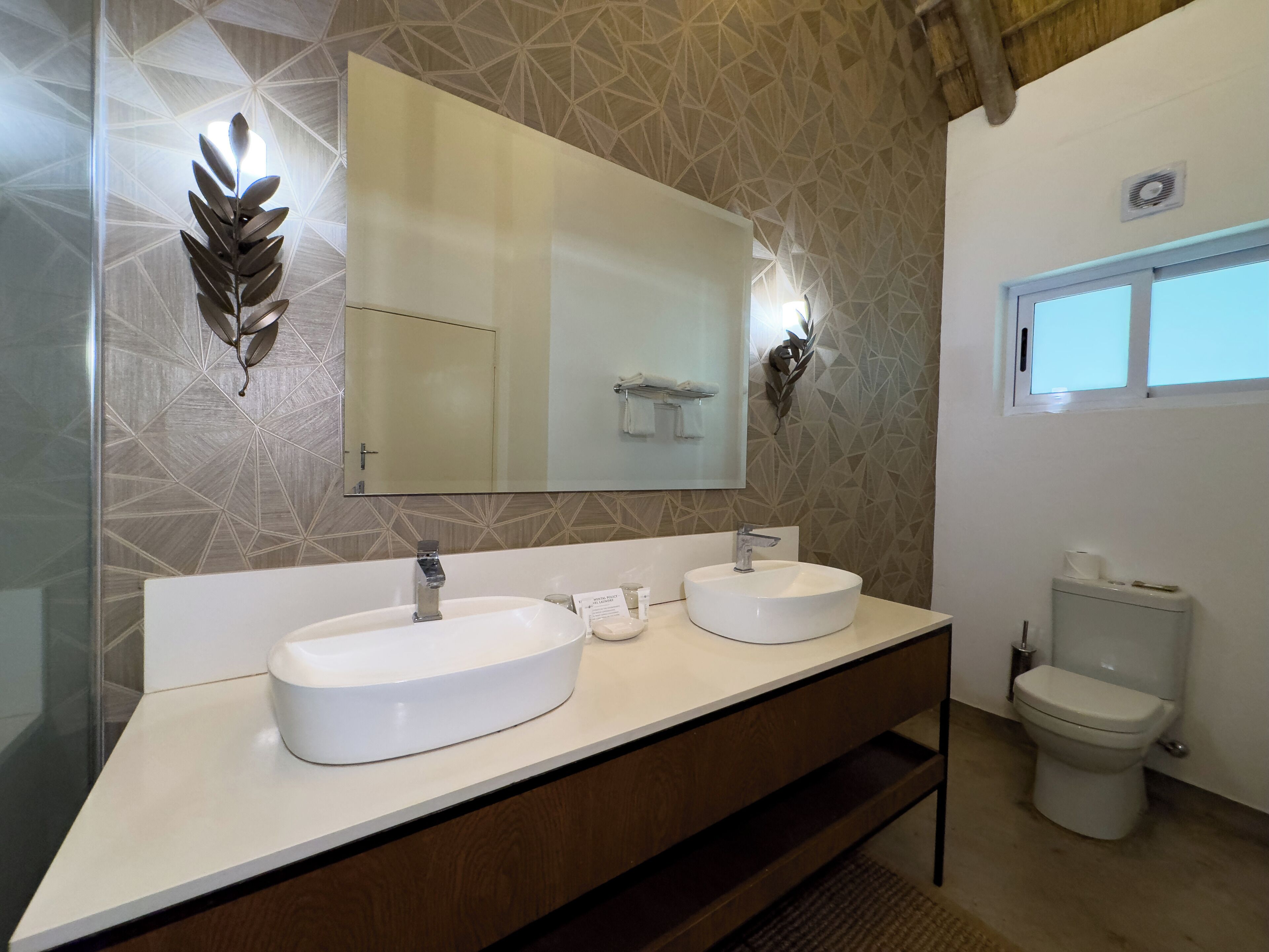 A modern bathroom with two sinks, a large mirror, and a toilet.