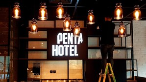 A hotel interior with a prominent 'PENTA HOTEL' sign, multiple hanging pendant lights, and a person on a ladder. - Pentahotel Hong Kong, Tuen Mun (Tuen Mun)