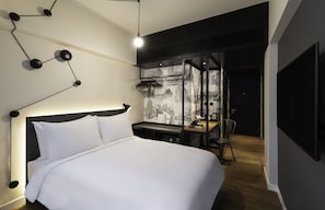 Een moderne hotelkamer met een groot bed, een bureau en een stoel. Op de muur zit behang met een stadsgezicht en er hangt een zwart plafondlamp.