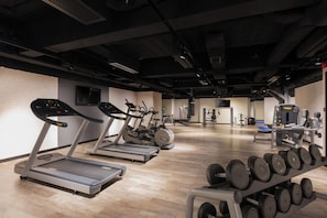 Een sportschool met loopbanden, krachttoestellen en een dumbbells rek.