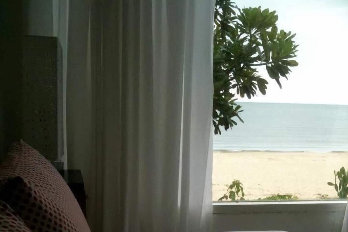 A hotel room with a bed, a window with curtains, and a view of the beach.