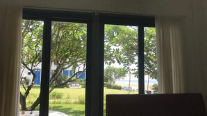 Habitación con un amplio ventanal que ofrece vista a un área verde, un árbol y un edificio con puerta azul.