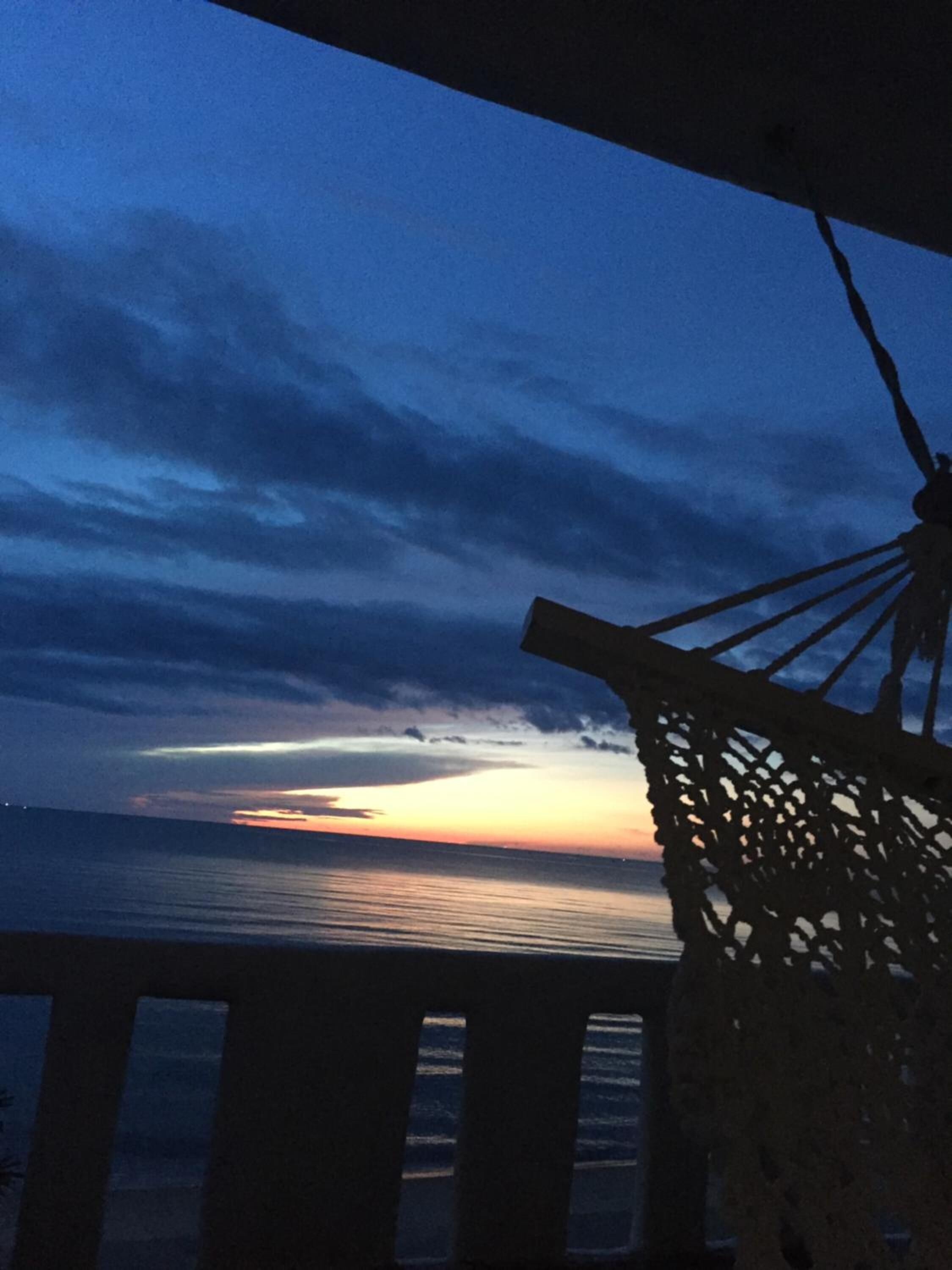 A sunset view from a balcony with a railing and a decorative hanging light fixture.