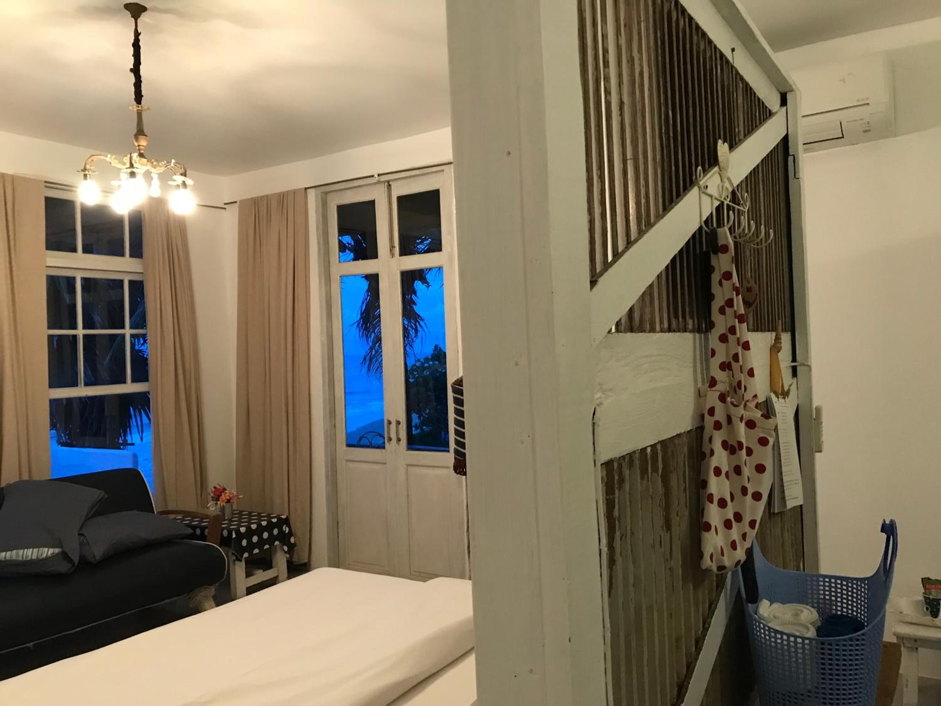 A room with a bed, a desk, a chair, a window with curtains, and a chandelier.