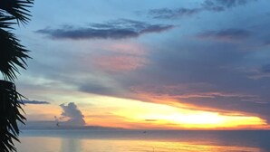Una playa con un atardecer sobre el agua, palmeras y un cielo despejado.