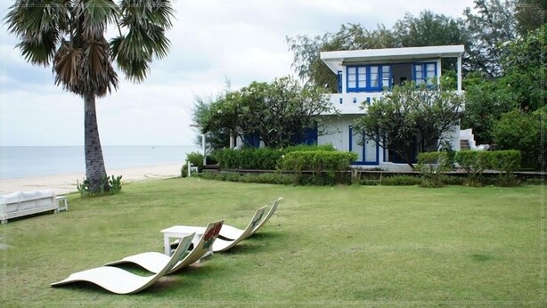 Una casa moderna con piscina y sillones de descanso en un césped.