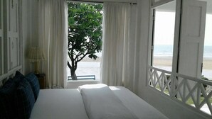 Un dormitorio con cama, mesita de noche, lámpara y vistas a la playa desde una ventana.