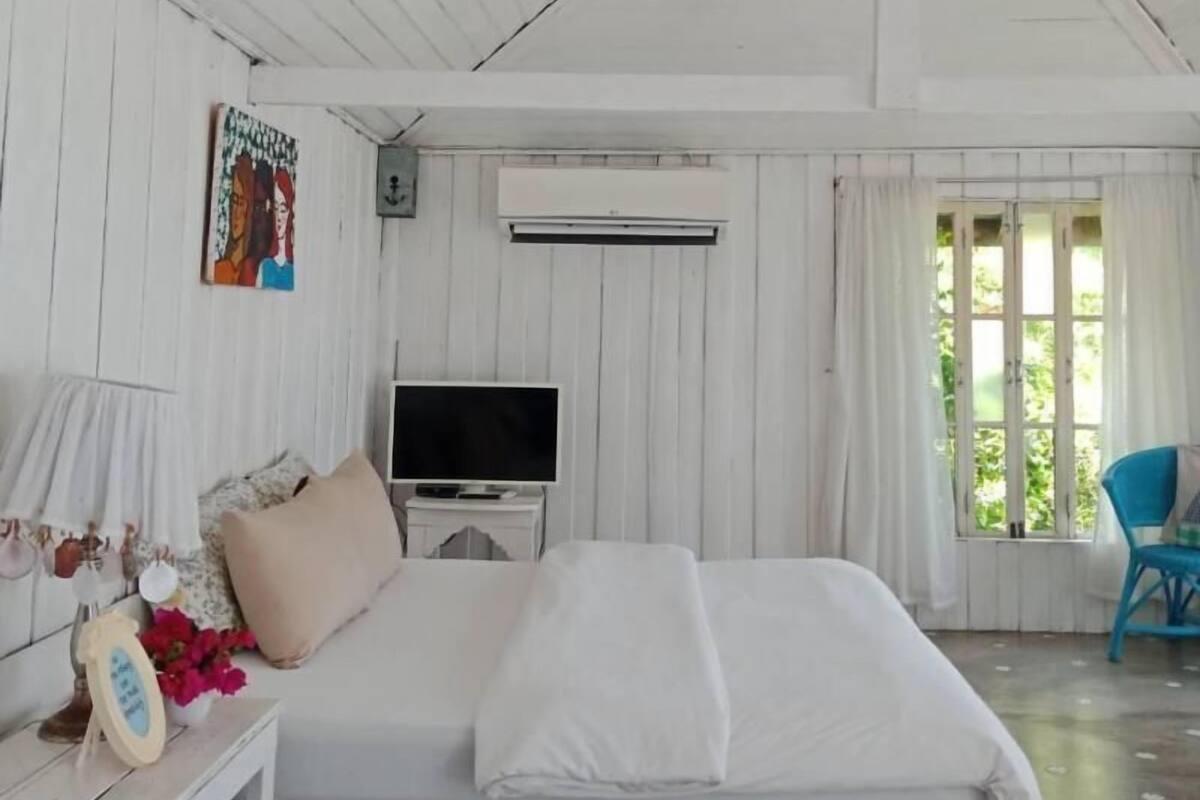 A bedroom with a bed, a TV, a small table with a lamp, and a chair.