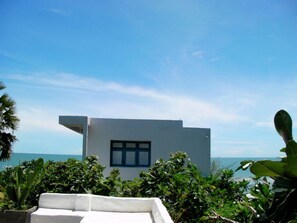 Un edificio moderno con un ventanal grande, rodeado de exuberante vegetación y vistas a un cuerpo de agua.