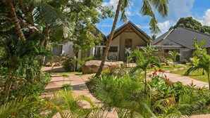 Un resort tropical con dos edificios principales, abundante vegetación y cielo despejado.