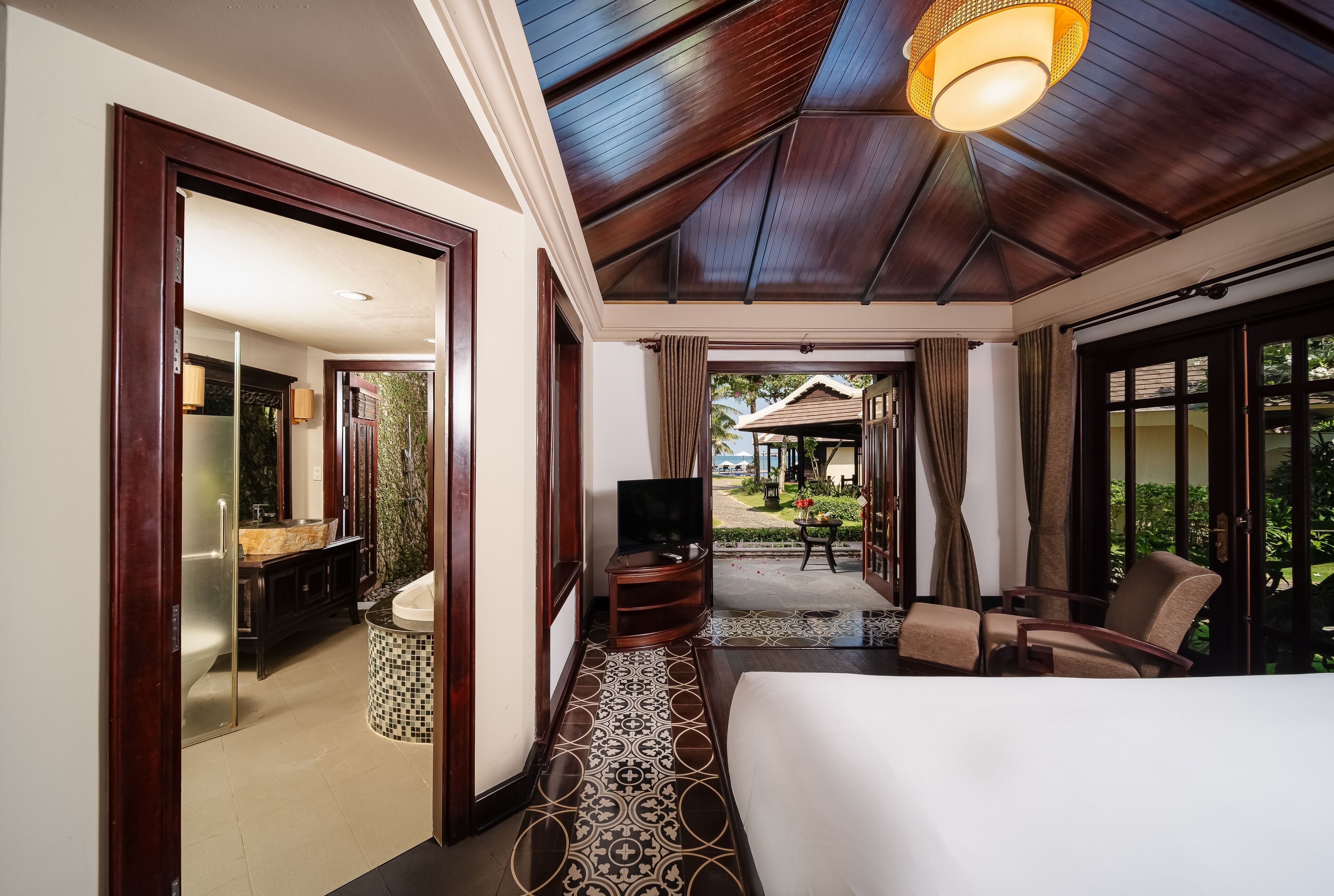A hotel room with a large bed, a TV, a bathroom with a mirror and sink, and a view of the garden.