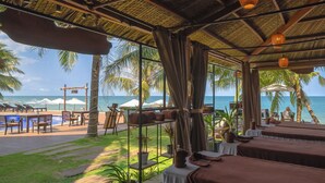Un resort frente a la playa con piscina, sillas de descanso y mesas bajo techo de paja.