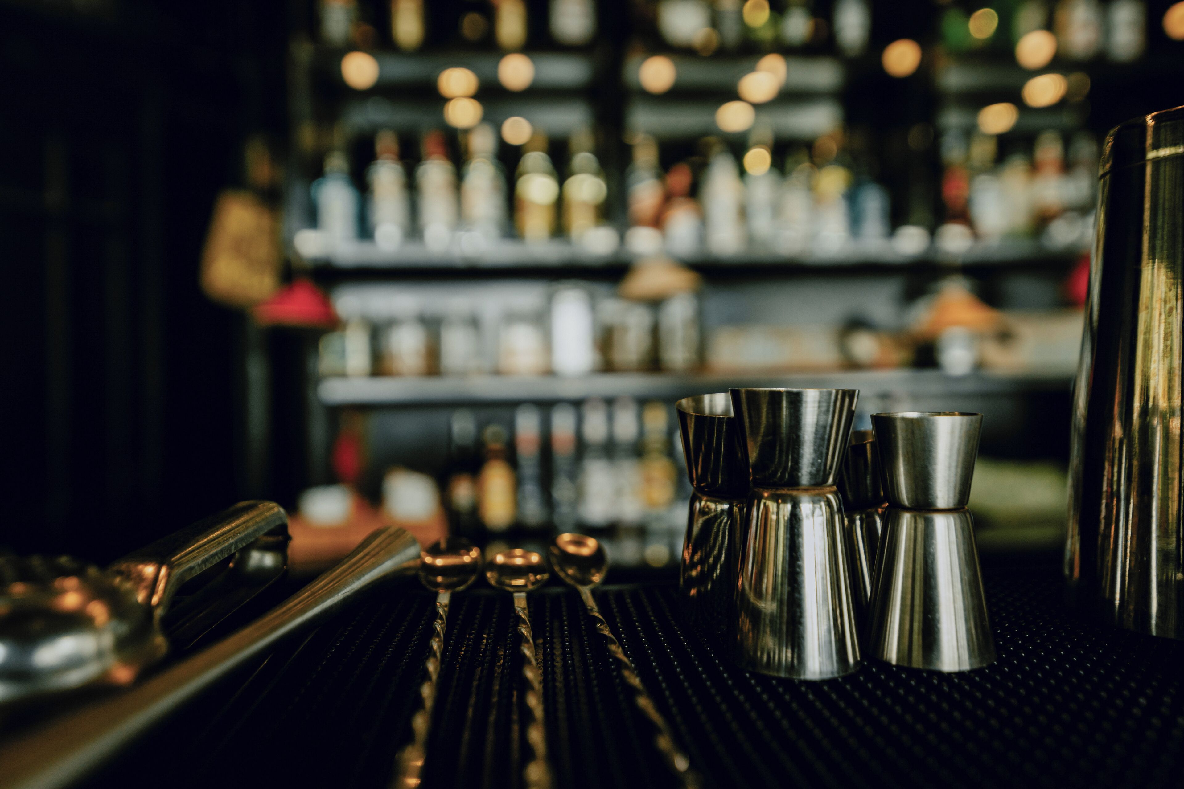 Una zona de bar con utensilios de acero inoxidable y botellas al fondo.