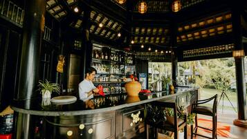 Uma área de bar com um bartender, prateleiras cheias de garrafas e um vaso grande.