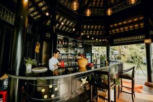 Uma área de bar com um bartender, prateleiras cheias de garrafas e um vaso grande.