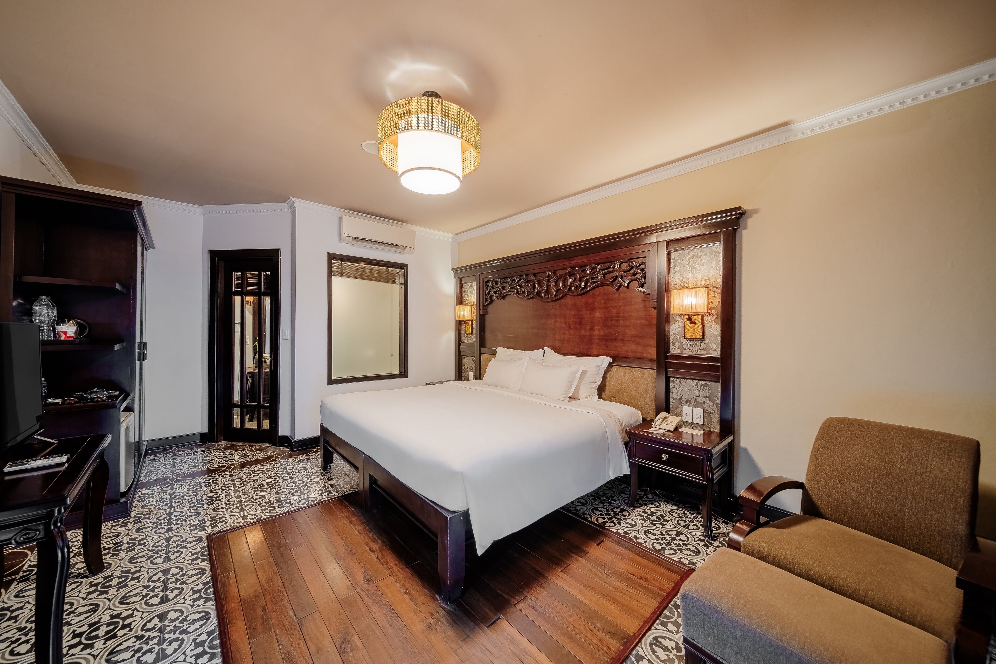 A hotel room with a large bed, a wooden headboard, a desk with a chair, and a television.