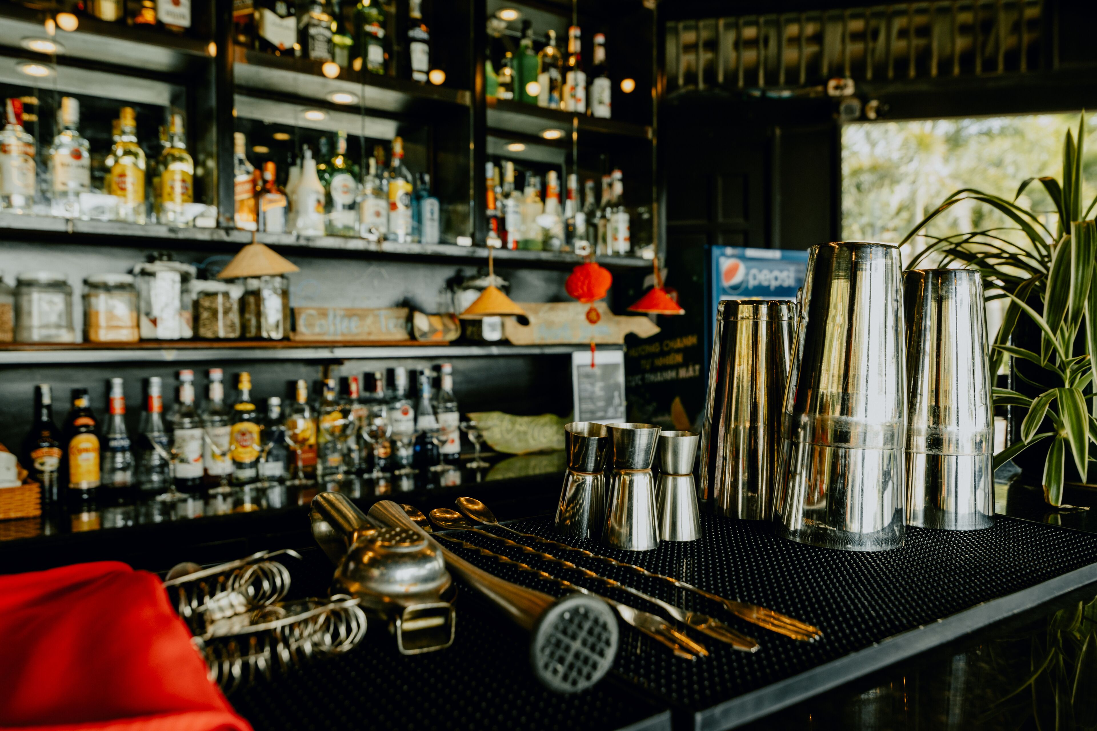 A bar area with various bottles and bar tools, including shakers and a pepsi sign.