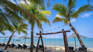 Una playa con palmeras, sillas de descanso y un columpio.