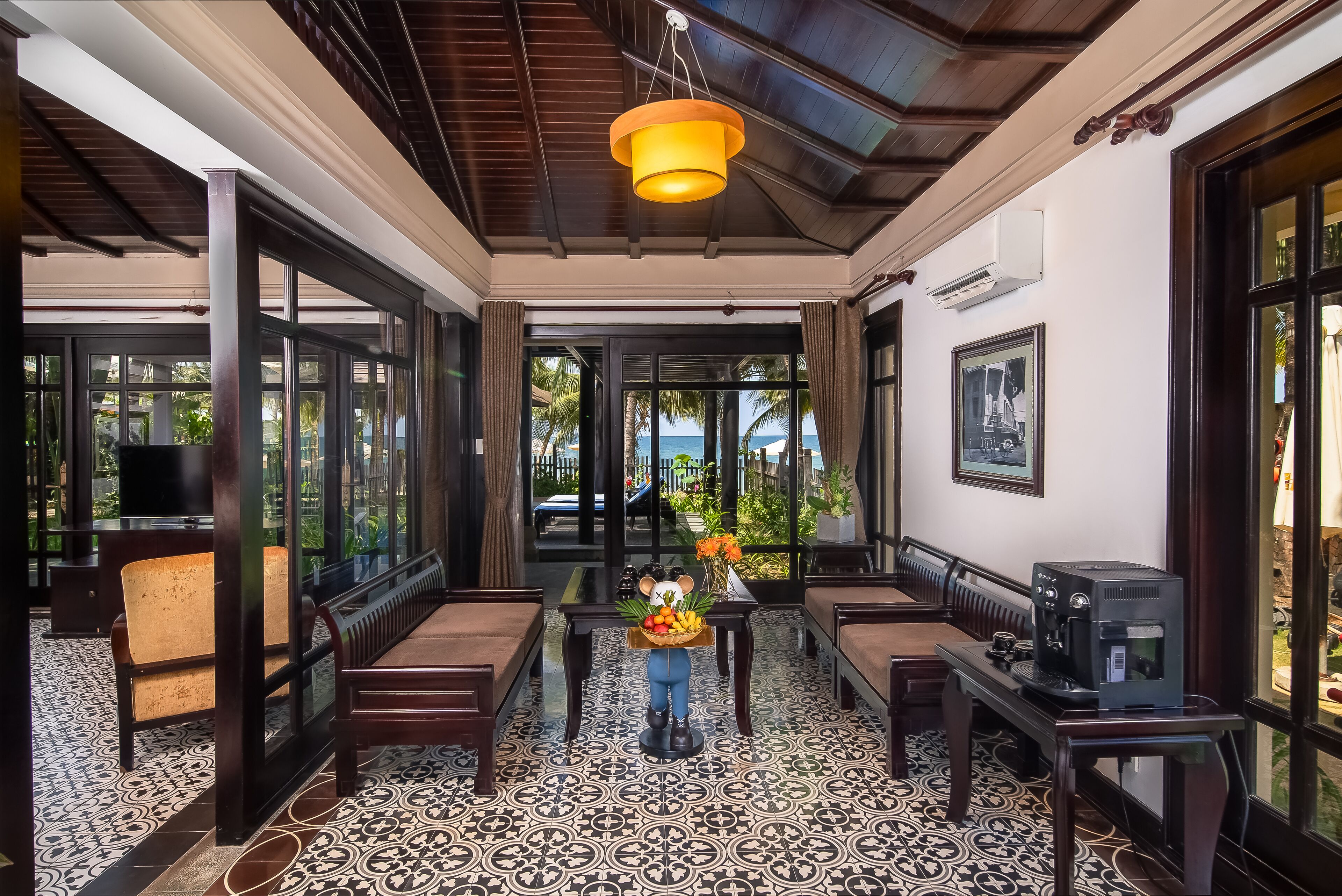 A room with a tiled floor, wooden furniture, a table with a fruit basket, and a coffee machine.