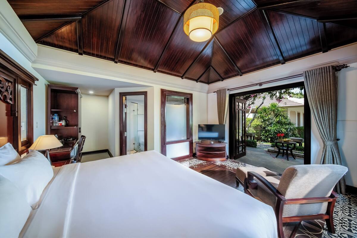Una camera d'albergo con un letto grande, una televisione, una scrivania e vista sul giardino esterno.