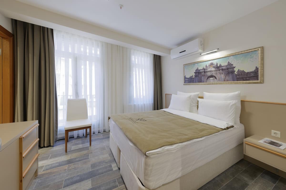 A hotel room with a bed, a chair, a desk, and a painting on the wall.