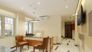 A hotel lobby with a reception desk, two wooden chairs, a television mounted on the wall, and a tiled floor. - Nishant Boutique Hotels (Istanbul)